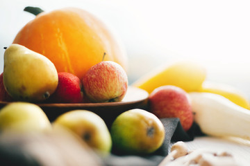 Pumpkin and zucchini in stylish wooden plate with apples and pears on linen apron on white wooden table in light. Space for text. Hello autumn concept and Fall Harvest