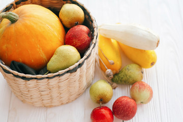 Happy Thanksgiving. Pumpkin and zucchini in stylish straw basket with apples and pears on white wooden background in light, Space for text. Fall Harvest and hello autumn concept