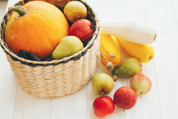 Happy Thanksgiving. Pumpkin and zucchini in stylish straw basket with apples and pears on white wooden background in light, Space for text. Fall Harvest and hello autumn concept