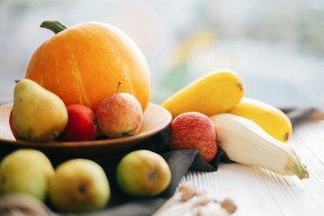 Hello autumn concept and Fall Harvest. Pumpkin and zucchini in stylish wooden plate with apples and pears on linen apron on white wooden table in light. Happy Thanksgiving