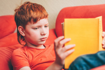 Cute red-haired boy with enthusiasm reads the book novel