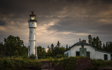 Lighthouse on bluff with trees and cloudy sky