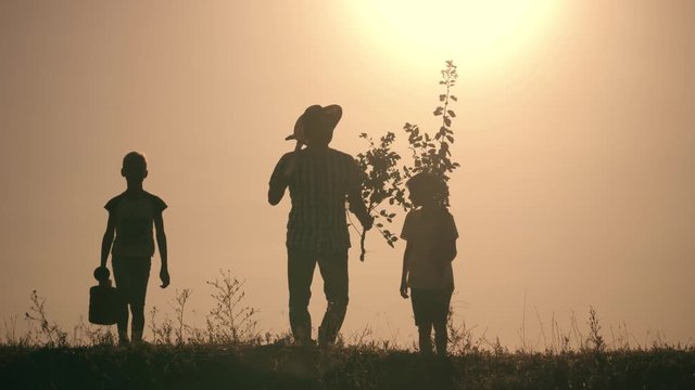 A happy family. Father and two sons plant and water the tree in the park at sunset. The concept of a happy family