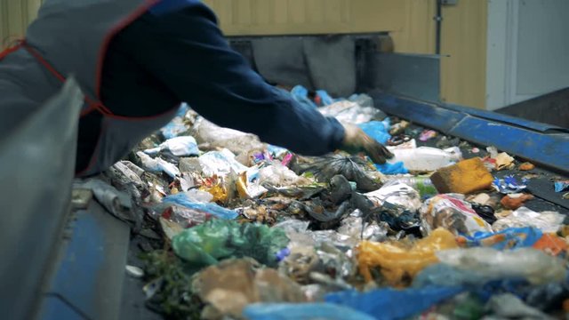 Garbage recycling plant. A person in gloves picks unrecyclable trash from a moving line at a waste sorting factory.