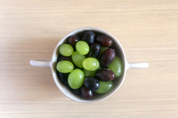 Artisan ceramic bowl filled with various types of grapes. Top view.

