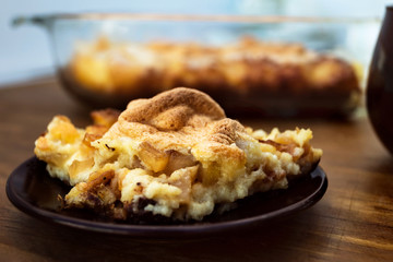 Serving casserole of apples, cottage cheese, semolina and cheese on a plate close-up on a wooden background.
