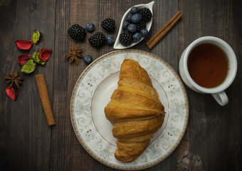 A cup of black tea with a fresh golden croissant and berries. on a wooden background. fresh bakery.