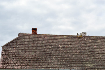 The old ancient sloping triangular roof of the house, the cottage is dirty with tusks overgrown with moss against the blue sky