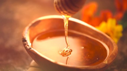Honey dripping from honey dipper in wooden bowl. Healthy organic thick honey closeup. Slow motion. 3840X2160 4K UHD video footage