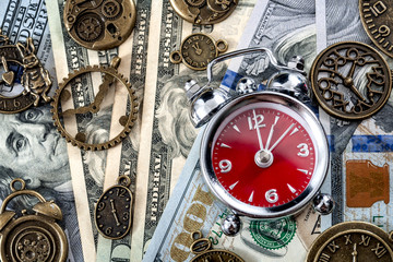 Fototapeta premium Time is money concept with flat lay of alarm clock on dollar bill or notes and surrounded by metal clocks