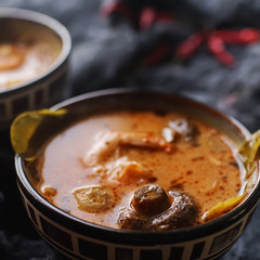 Tasty asian soup tom yam in small bowls with chilli pepper, shrimp, mushrooms, coconut and lime on a dark background, healthy food concept, selective focus