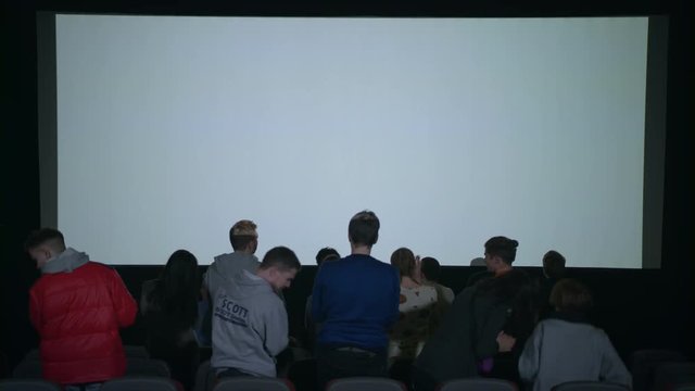 Spectators applaud film that ended. Movie is over. Audience leaving cinema applauding. Satisfied spectators applaud after movie session. End of movie. Audience leaving cinema. Movie ending screen