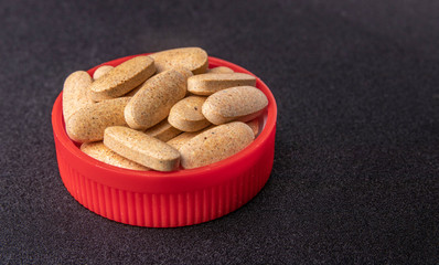 oval brown pills in a red lid on a dark blue background