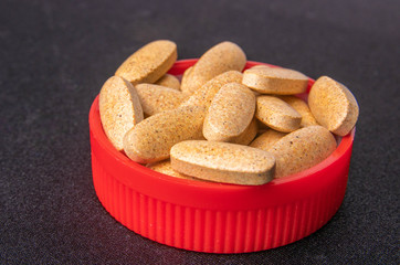 oval brown pills in a red lid on a dark blue background