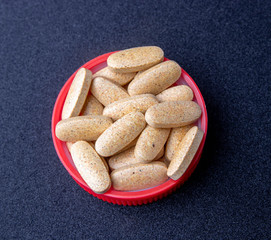 oval brown pills in a red lid on a dark blue background