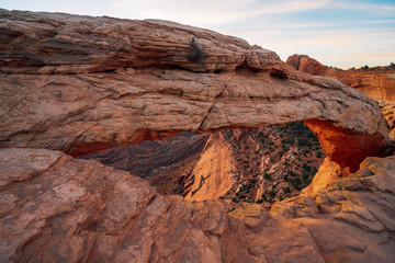 Fototapeta na wymiar Cliff's-edge sandstone Mesa Arch framing an iconic sunrise view of the red rock canyon landscape below.