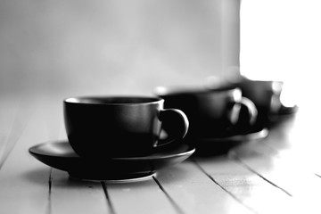The black and white image of hot coffee in black glass is placed on a wooden table waiting for drinker to bring it to his table during the break.