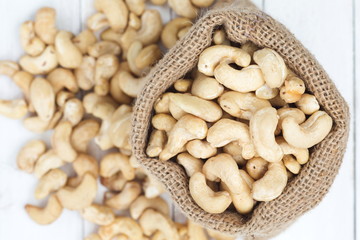 Pile of cashew nuts in sackcloth pouch on white wooden desk.