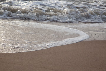 Sand beach with sea waves in the sunset.