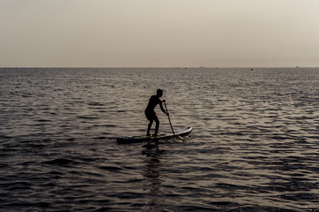 Fototapeta na wymiar Paddle standing, silhouette of man on the beach at sunset. SUP surfing.