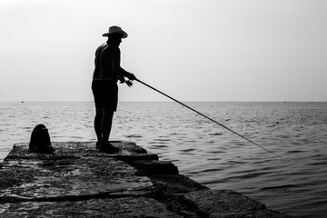 Fisherman standing on a pier at dawn sky background. Silhouette photo.