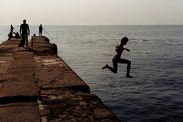 Fototapeta premium People rest on the pier. Silhouette photo. The fisherman is fishing. The girl jumped into the water.