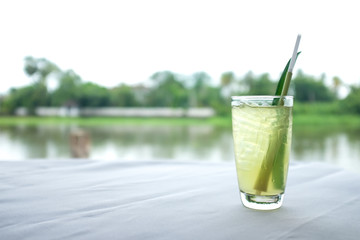 A glass contains refreshment drink and a straw on a white sheeted table with river background