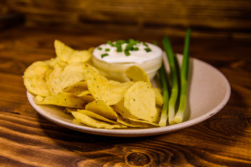 Ceramic plate with potato chips and glass bowl with sour cream on wooden table