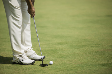 Golf player at the putting green hitting ball into a hole