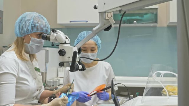 Doctor used microscope. Dentist is treating patient in modern dental office. Orthodontist works with an assistant. The operation is carried out using cofferdam. The client is inserted and restored