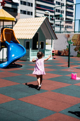 little toddler girl in pink dress running around playground, with her back to the camera, during a summer day