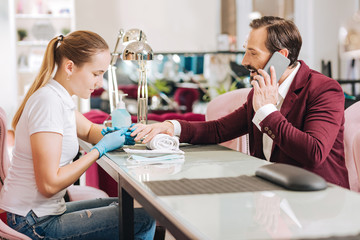 While manicuring. Woman giving manicure and vigorous mature man gossiping on phone