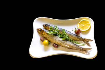 Smoked sprats or Baltic herring on white dish served with vegetables and greens isolated on black background