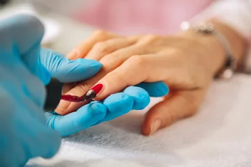Fototapeten Classic red. Close up of female hands applying nail polish and togging blue gloves © zinkevych
