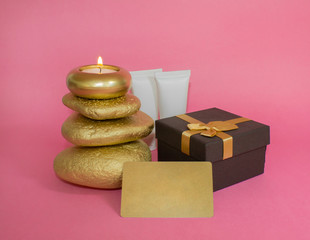 Gift set. Candle on stones, cosmetics, gift box and gift card. On a pink background.