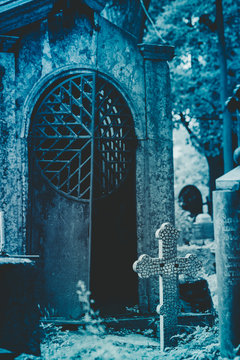 The slightly open iron door of the old crypt in the cemetery at night. The concept of Halloween and Death. Moody blue toned.