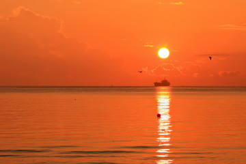 Beautiful red orange sunrise above the sea and clouds with a ship crossing the reflected in the water sun path