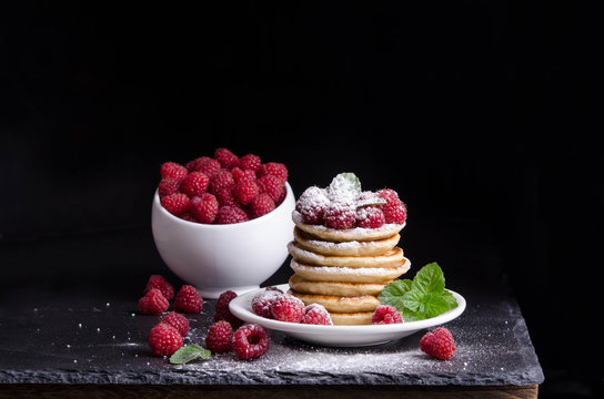 Bowl and  Pancakes with raspberries around on black backgound