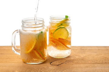 glass mason jars of pouring homemade lemonade with sliced fresh lemon, orange, lime, twig mint and bubbles on wooden background isolated