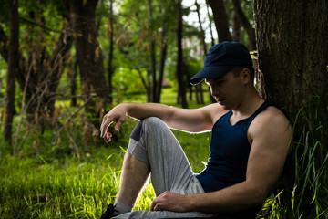Naklejka na ściany i meble Attractive fitness man sitting near tree in the park
