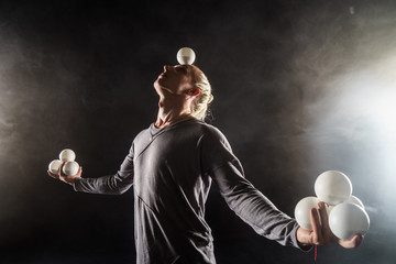 Blond juggler keep in balance white balls on black background