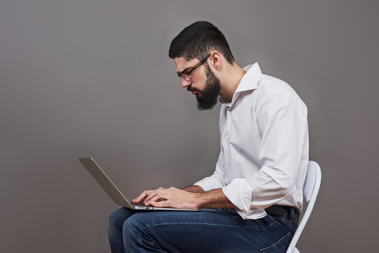 Handsome Business Man In Glasses And Suit Holding Laptop In Hands And Writing Something. Side View. Isolated Gray Background