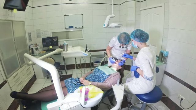 Woman at dentist clinic gets dental treatment to fill a cavity in a tooth. Dental restoration and composite material polymerization with UV light and laser. Shooting at a wide angle.
