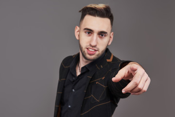 Young smiling man in formal wear pointing with finger on you, looking at camera, isolated on gray background