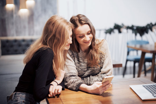 One-on-one meeting.Two young business women sitting at table in cafe.Girl shows her friend image on screen of smartphone. On table is closed notebook.Meeting friends