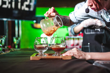 women's hands professionally barista pour the prepared drink into glass cups. championship among coffee houses, members of teams show barista's skill, prepare drinks, teamwork.