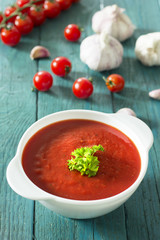 Creamy tomato soup with parsley and garlic on a blue kitchen table 