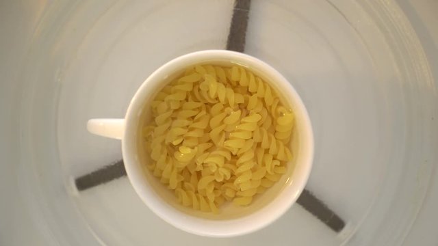 Making microwave mug meal. Boiling pasta in a mug. Microwave macaroni with water top view.