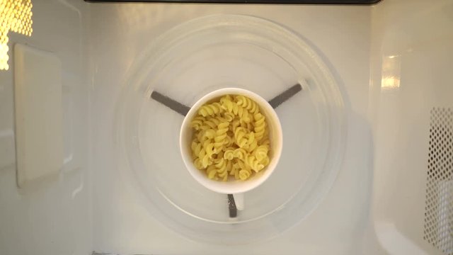 Making microwave mug meal. Boiling pasta in a mug. Microwave macaroni with water top view.