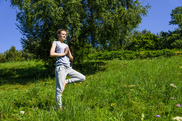 Young attractive woman practicing yoga outdoors on a sunny day, Vrikshasana (tree pose)